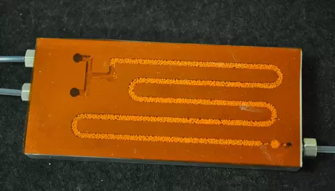 Typical NIST microreactor plate for studying enzyme catalyzed polymerization. The aluminum plate, topped with a transparent film, is approximately 40 mm by 90 mm centimeters.