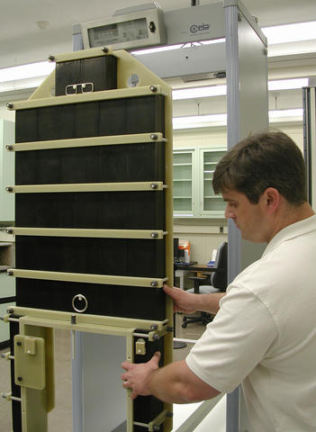 Guest researcher John Jendzurski prepares the NIST electromagnetic phantom for passage through the walk-through metal detector behind it.