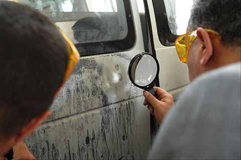 Law enforcement officers locating latent fingerprints on the side of a van.