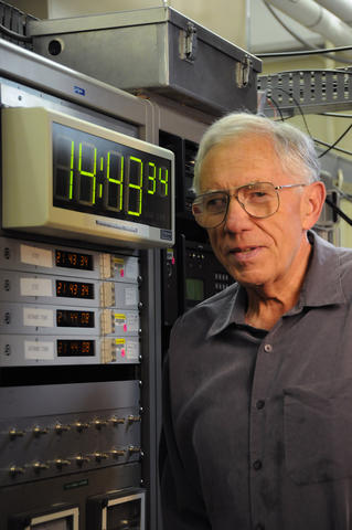 Man with gray hair standing beside computer with digital clock display