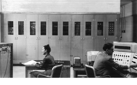 Lady on left and man on right at desks facing lab equipment