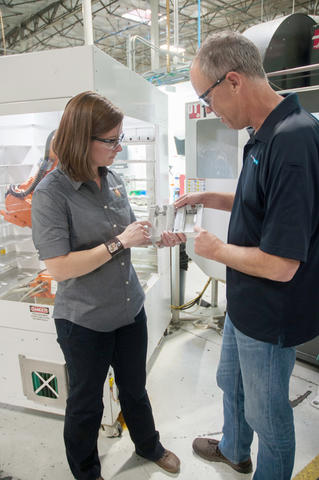 A man and a woman examine a part on a manufacturing floor