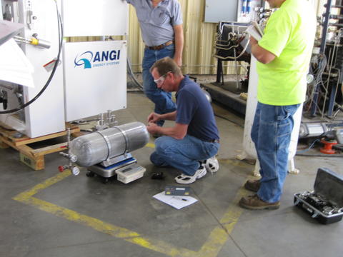 NIST Office of Weights & Measures’ Richard Harshman kneeling to inspect a grey canister holding natural gas