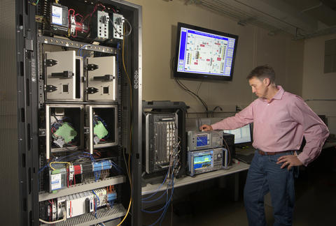 NIST engineer Rick Candell is seen monitoring the strength and clarity of a wireless signal run through a virtual factory environment (a graphic of which is seen on a monitor above Candell's head).