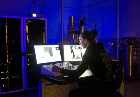 Alex Curtin at the controls of the helium-ion microscope, shown at rear. The racks to her left house the electronics for the instrument.