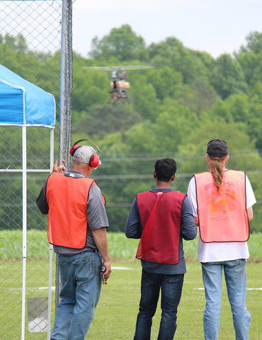 three men with their backs to the camera operate a drone hovering in the background