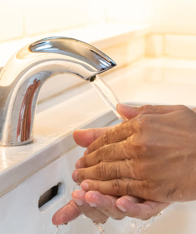 Man washing his hands in a public restroom using a automatic sensor faucet.