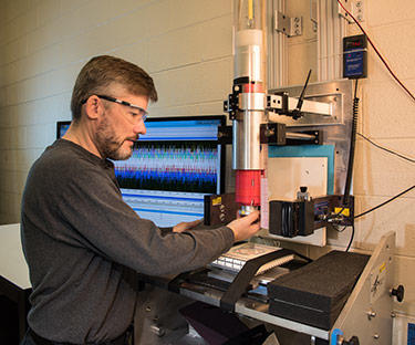 NIST Materials Scientist Michael Riley prepares a sample of material for a drop test that will reveal its ability to absorb and dissipate energy.