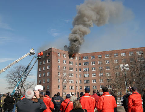 High rise building with smoke coming out of upper windows. Two people in bucket trucks.