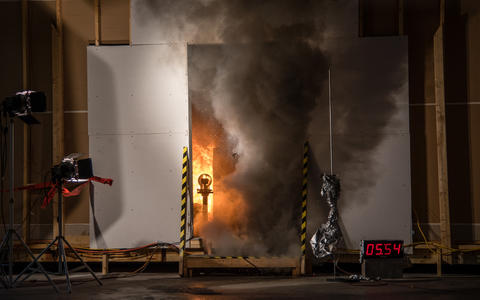 smoke billows from the open doorway of a burning test storage room