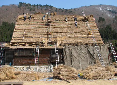 Workers are seen building a thatched roof on Japanese house.