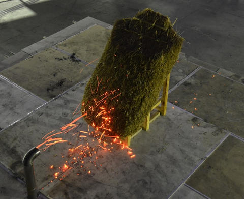 A rectangular-shaped model of a thatched roof is attacked by embers emitted from the pipe-shaped mouth of the NIST Dragon device.