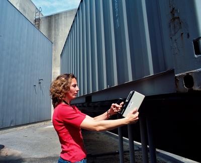 Woman stands holding a radiation detection device in front of a truck