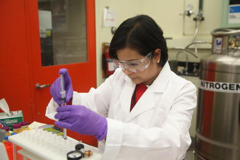 A woman with goggles prepares a sample near a large instrument.