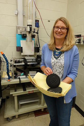 Woman stands in a lab holding two black round disks