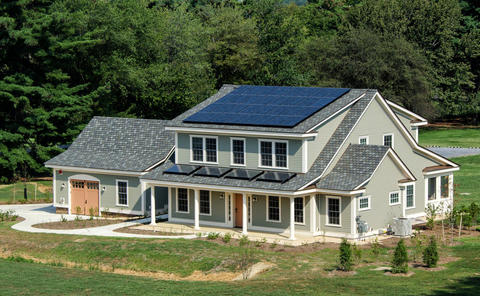 Photograph of large residential-style home with blue tile roof and solar panel in suburban campus setting.