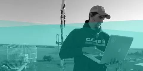 farmer stands in a field using a laptop