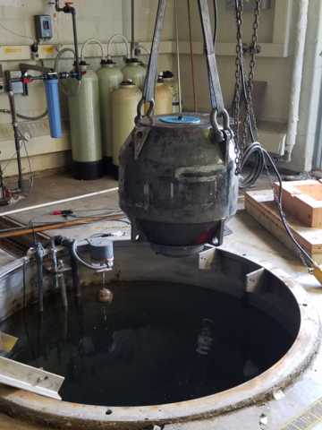 A large metal ball is pulled out of a pit with an overhead pulley