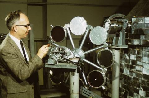 A man in a suit stands next to a piece of equipment with round targets.