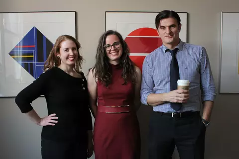 Amanda Brown, Meridith Wentz, and Eugen Ghenciu, respectively, stand close together in a hallway with framed artwork behind them, facing the camera and smiling.