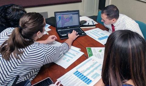 small group of people at a conference table looking at a laptop screen