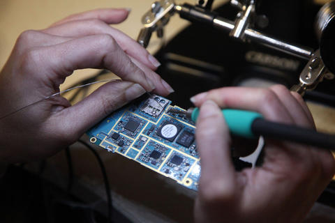 A close-up photo of a person's hands as they use a soldering iron to attach wires to a circuit board.