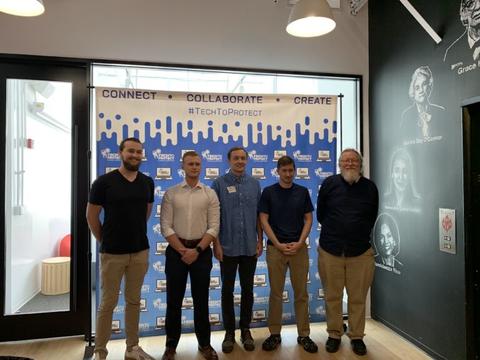 This image shows a ggroup of five men standing in front of a Tech to Protect sign.