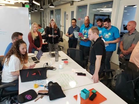 A team from September's challenge huddles around a table looking at a computer.