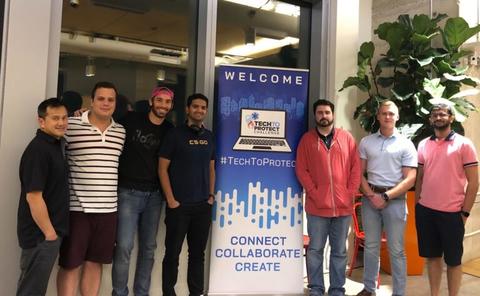 This image shows a group of people standing by a "Welcome" sign for the Tech To Protect Challenge