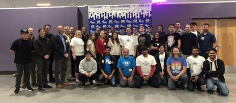 This image shows a group of challenge participants standing in front of Tech to Protect sign with the words "Connect", "Colloborate", and "Create"