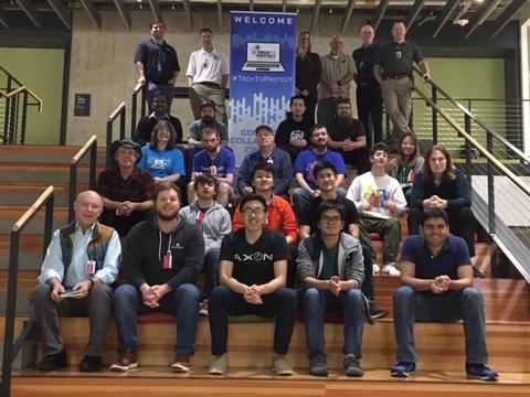 This image shows a group of challenge participants standing and sitting in front of a Tech to Protect challenge sign that says "Welcome" and "#TechToProtect"