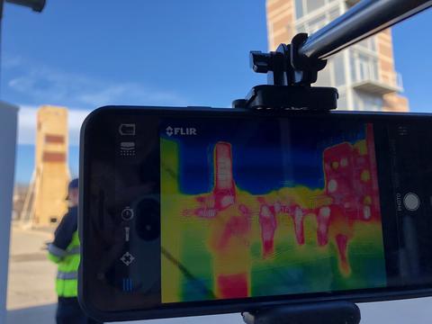 A phone mounted on a metal arm shows a thermal image of several people standing in demo area. 