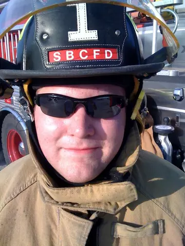 This image shows a man in firefighting uniform, wearing sunglasses