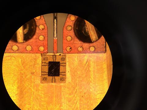 Photodiode Flat, round shape in various shades of orange color, with copper wiring and other decorations covering the top third and a small, square black object surrounded by a gold frame in the center.
