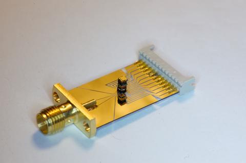 Gold-colored rectangular device with cylindrical attachment on one end. 