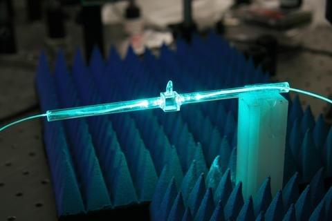 A glowing blue cylindrical rod has fibers coming out of either end. 