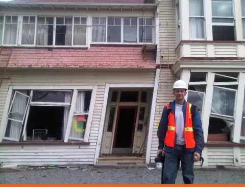 NIST research structural engineer&nbsp;Matthew Speicher inspecting damage after the 2011 earthquake in Christchurch, New Zealand. He is standing in front of a building which has structural damage making it lean to left.
