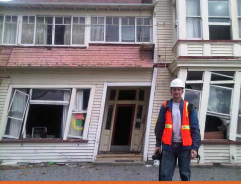 NIST research structural engineer Matthew Speicher inspecting damage after the 2011 earthquake in Christchurch, New Zealand. He is standing in front of a building which has structural damage making it lean to left.
