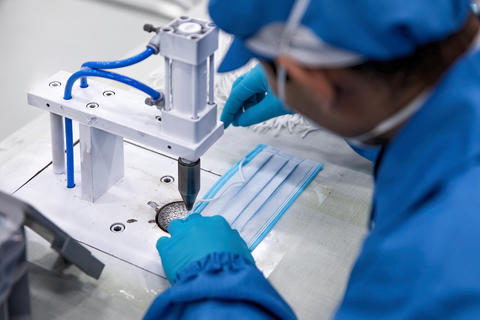 A person leans over a sewing machine to work on a protective face covering. 