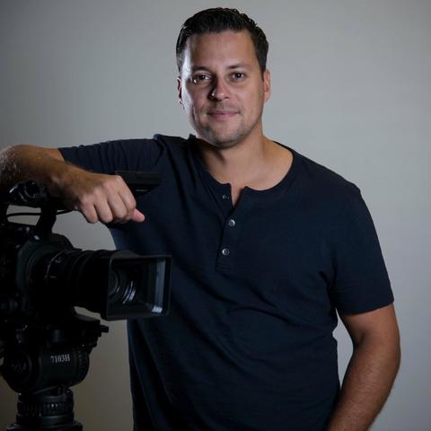 Man standing with an arm leaning on a video camera