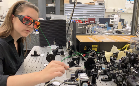 woman with red laser safety glasses on working at a laser table adjusting optics