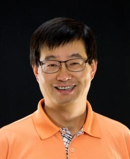 headshot of man in orange shirt. black background.