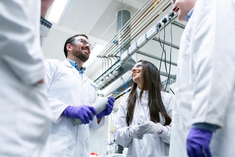 four scientists standing, facing each other, collaborating on a new device