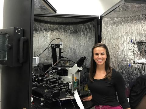 A woman (Callie Higgins) stands in front of a piece of photopolymerization equipment. 