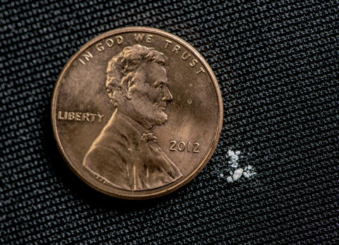 Black background. Photo of a penny. Next to the penny is a tiny amount of a white powder.