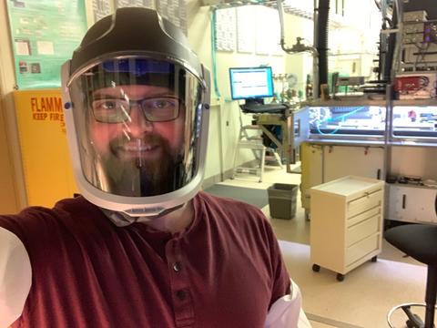 A man wearing a safety visor poses in front of lab equipment. 