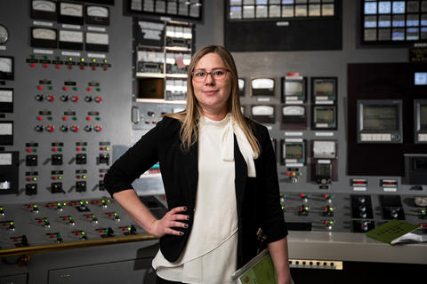 A woman stands in front of a wall full of knobs and switches.