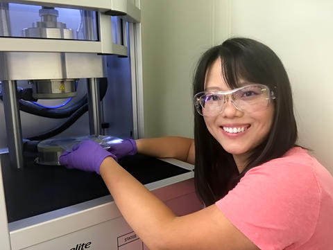 A woman wearing safety goggles reaches under a scientific device. 