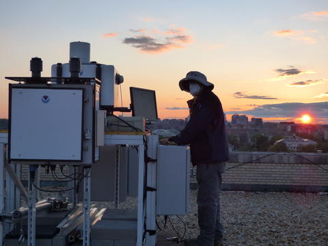 Man standing next to equipment on top of building during a sunset.  