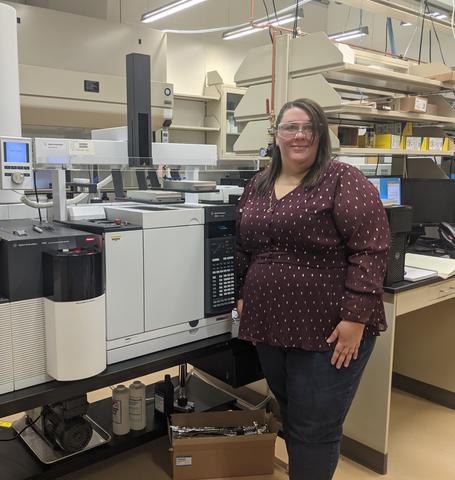 Cheryle Beuning poses in front of scientific equipment, wearing safety goggles.